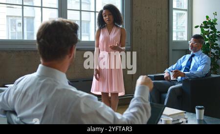 Femme d'affaires dirigeant la réunion informelle avec l'équipe multiculturelle assise sur des canapés dans le bureau moderne Banque D'Images