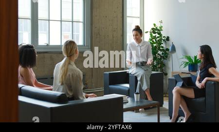 Jeune femme d'affaires menant une réunion informelle avec l'équipe féminine assise sur des canapés dans le bureau moderne Banque D'Images
