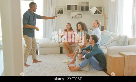 Groupe de jeunes amis à la maison assis sur le sol s'amusant à jouer des charades ensemble Banque D'Images