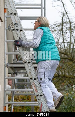 Malerin steigt auf eine Schiebeleiter hoch am Giebel eines Hauses. Vorarbeiten zum Malern des Dachüberstands, modèle libéré für redaktionelle Nutzung, Dachüberstand streichen *** peintre monte une échelle coulissante sur le pignon d'une maison travaux préparatoires pour peindre le surplomb du toit, modèle libéré pour usage éditorial, peindre le surplomb du toit 20241105-DSC 8782 Banque D'Images