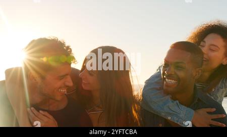 Gros plan sur le groupe de jeunes amis ayant une course de piggyback sur Winter Beach avec Lens Flare Banque D'Images