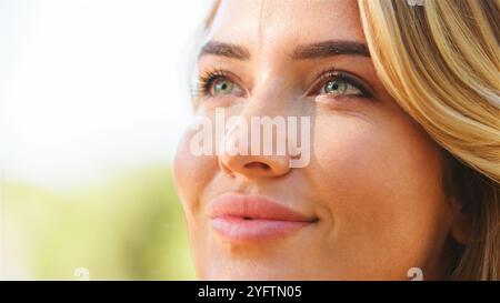 Une jeune femme aux cheveux blonds clairs regarde vers le haut, absorbant la lumière chaude du soleil. Son expression calme reflète un moment de tranquillité au milieu d'un embellissement Banque D'Images