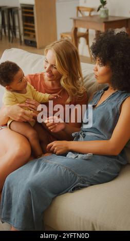 Dans un salon chaleureux et accueillant, deux femmes profitent de moments de qualité avec un bébé. Une femme tient l'enfant tandis que l'autre est assise près, les deux sourires Banque D'Images