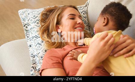 Une mère chérit une interaction joyeuse avec son bébé tout en se reposant confortablement sur un canapé moelleux. Leurs sourires rayonnent de chaleur et d'affection, mettant en valeur Banque D'Images