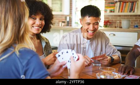 Un groupe d'amis est rassemblé autour d'une table en bois, engagé dans un jeu de cartes animé. Le rire remplit l'air alors qu'ils partagent des collations et des boissons, créant Banque D'Images