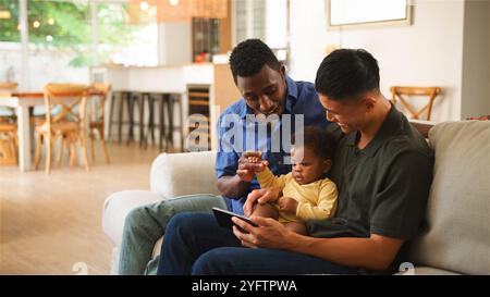 Deux hommes et un bébé s'engagent avec une tablette dans un environnement lumineux et accueillant. Banque D'Images