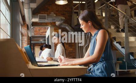 Femme d'affaires travaillant dans le bureau multiculturel moderne écoutant de la musique sur des écouteurs ou des écouteurs Banque D'Images
