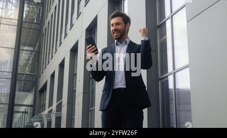 Homme d'affaires caucasien homme d'âge moyen homme d'affaires adulte homme homme entrepreneur employeur dans l'immeuble de bureaux du centre-ville gagner le téléphone mobile atteindre la victoire Banque D'Images