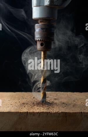 gros plan du trou de forage avec foret émoussé dans le bois dur avec de la fumée et brûlant, générant une chaleur excessive endommageant le bois, doux focus avec le mouvement Banque D'Images