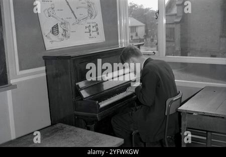 Années 1950, historique, un écolier plus âgé assis dans un coin d'une salle de classe jouant du piano, Angleterre, Royaume-Uni. Banque D'Images