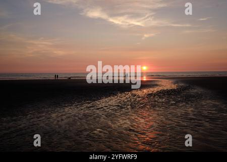 Coucher de soleil rouge brillant sur la mer à Ynslas sur la côte galloise, Cardigan, pays de Galles. Les vacanciers profitent de la soirée ensoleillée d'été. Banque D'Images