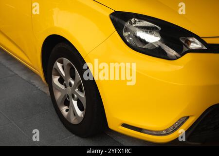 Phares de voiture et partie de roue montrant. Vue avant de la nouvelle voiture de luxe moderne jaune garée à l'extérieur. Phares et détail de roue de voiture jaune Banque D'Images