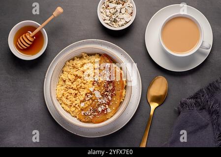 Photographie alimentaire de bouillie de millet avec banane caramélisée, noix de pécan, noix, flocons de noix de coco, chia, graines de lin, miel, thé au lait d'amande Banque D'Images