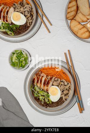 Photographie alimentaire de soupe ramen avec poulet, soba, nouilles de sarrasin, œuf, champignon, oignon de printemps et carotte, toasts, baguettes Banque D'Images