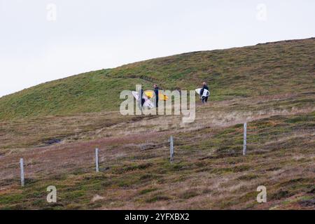 1er novembre 2024. Dunnet Head, Écosse. Deux surfeurs masculins et une surfeuse remontant un promontoire à Dunnet Head près de Thurso, en Écosse. Banque D'Images