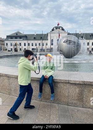 Deux jeunes garçons s'engagent dans une séance de photographie ludique près d'une fontaine contemporaine sur une place urbaine de Bratislava, capturant des souvenirs et s'amusant Banque D'Images