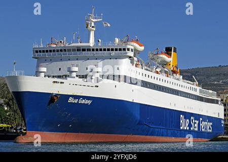 Symbolbild Fähre Blue Galaxy der Blue Star Ferries, massiver Weiß-blauer Rumpf mit großem Schriftzug, oberes Deck mit Rettungsbooten, markanter gelber Schornstein, bereit für Passagier- und Fahrzeugtransport, strahlender Himmel und Küstenlandschaft im Hintergrund *** image symbolique ferry Blue Galaxy of Blue Star Ferries, énorme coque bleue blanche avec de gros lettrage, pont supérieur avec canots de sauvetage, entonnoir saisissant, ciel jaune et paysage de transport, Hans Juberx Banque D'Images