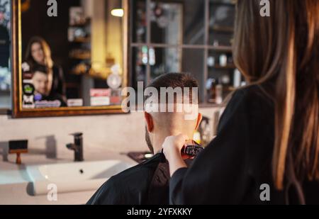 Jeune femme coiffeuse faisant la coiffure de coupe de cheveux de coupe de coupe de cheveux d'hommes à l'aide de coupe de cheveux Clipper miroir opposé magasin de coiffure de style moderne. Service de soins capillaires local sma Banque D'Images