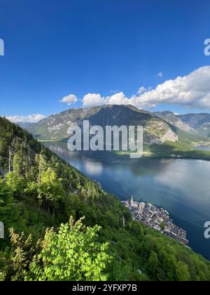 Un magnifique paysage alpin avec un village pittoresque niché par un lac Azur immaculé, entouré de collines verdoyantes et de montagnes majestueuses sous un Banque D'Images