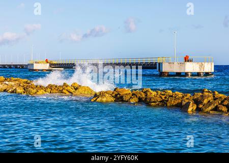 Des éclaboussures d'eau de mer contre des rochers près de la jetée brise-lames sous un ciel bleu clair sur la côte des Caraïbes. Curaçao. Banque D'Images