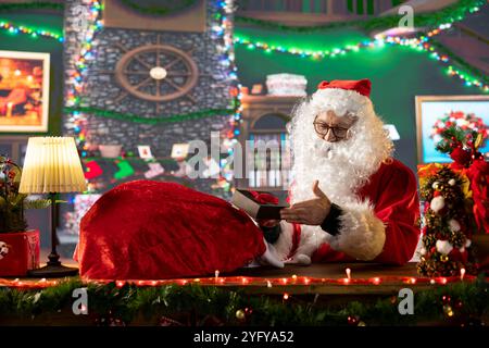 Vieil homme barbu blanc en costume attachant son sac plein de cadeaux, se préparant pour le voyage autour du monde. Répandre l'esprit des vacances d'hiver et surprendre les enfants, la tradition de Noël. Banque D'Images