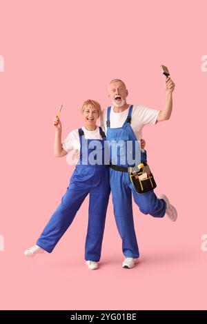 Couple mature de décorateurs avec des pinceaux sur fond rose Banque D'Images