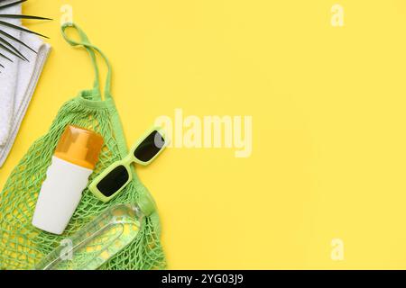Composition avec bouteille de crème solaire, sac à ficelle et lunettes de soleil sur fond jaune Banque D'Images