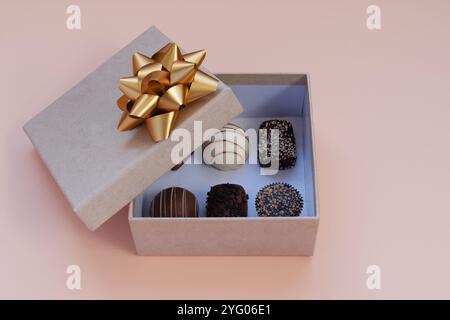 Boîte de chocolat gourmande avec arc doré sur fond pastel Banque D'Images