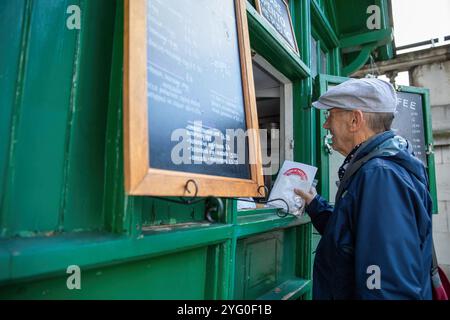 Londres, Royaume-Uni. 8 octobre 2024. Steve, un bénévole de Poppy Cab remet des tracts au propriétaire d'un refuge Green Hut, Cab Mans Shelter. Fondée il y a quinze ans par des chauffeurs de taxi londoniens, Poppy Cabs offre des trajets gratuits aux vétérans militaires participant au service annuel du jour du souvenir au cénotaphe de Westminster, à Londres. Inspirés par le Royal British LegionÃ-s Poppy Appeal, où les badges rouges du coquelicot sont échangés contre des dons caritatifs, ces chauffeurs de taxi dévoués s’organisent dans le cadre de l’initiative Ã¬Poppy CabsÃ®. Chaque année, les chauffeurs offrent des trajets gratuits aux vétérans à partir du train majeur Banque D'Images