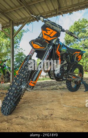 Balikpapan, Indonésie - 7 septembre 2024. Une moto de motocross 250cc noire et orange est garée sous un hangar, prête pour l'aventure. Banque D'Images