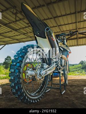 Balikpapan, Indonésie - 7 septembre 2024. Une moto de motocross noire et orange de 250cc vue de l'arrière, est garée sous un hangar, prête pour l'aventure Banque D'Images