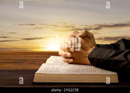 Homme priant avec ses mains sur une Bible sainte ouverte sur une table en bois. Symbole de foi et de culte en Dieu. Prières de christianisme des gens. Service religieux, Banque D'Images