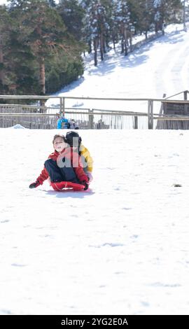 Deux enfants glissant avec un traîneau sur une colline enneigée dans les montagnes Banque D'Images