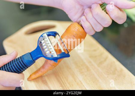 Mains de femme épluchant la carotte orange fraîche dans une cuisine Banque D'Images