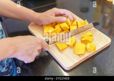 Mains de femme coupant la citrouille jaune fraîche dans une cuisine Banque D'Images