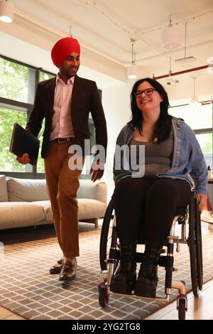 Homme d'affaires portant turban sikh et femme d'affaires sur fauteuil roulant au bureau Banque D'Images