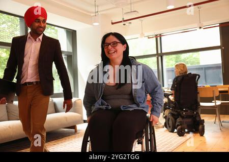 Homme d'affaires portant turban sikh et femme d'affaires sur fauteuil roulant au bureau Banque D'Images