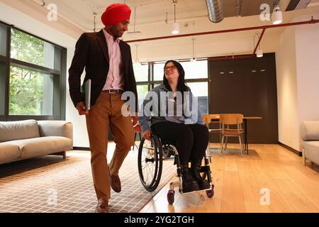 Homme d'affaires portant turban sikh et femme d'affaires sur fauteuil roulant au bureau Banque D'Images