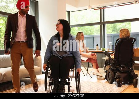 Homme d'affaires portant turban sikh et femme d'affaires sur fauteuil roulant au bureau Banque D'Images