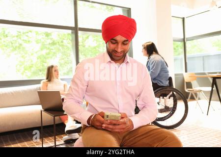 Homme d'affaires portant du turban sikh assis avec le téléphone dans le bureau Banque D'Images