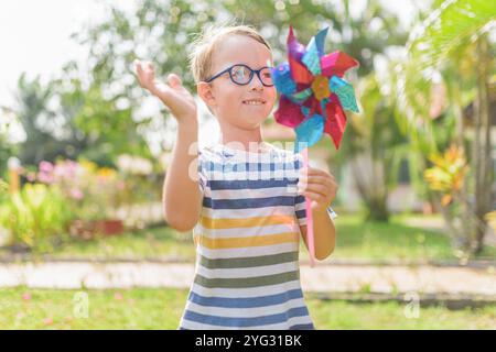 Garçon dans les lunettes joue avec la roue à épingles dans un jardin Banque D'Images