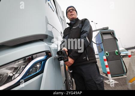 Hambourg, Allemagne. 06 novembre 2024. Rüdiger Düring, employé, se tient debout avec un câble de charge rapide sur un camion électrique 'Iveco S-eway' à côté d'une station de charge lors d'un événement de presse pour l'ouverture d'un hub de charge pour camions électriques au Cruise Center Steinwerder dans le port de Hambourg. Crédit : Christian Charisius/dpa/Alamy Live News Banque D'Images