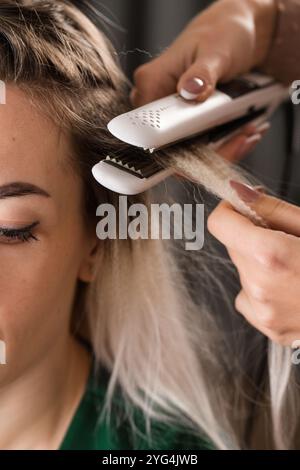 Un styliste utilise un fer à friser pour ajouter du volume aux cheveux d'une femme. Gros plan Banque D'Images