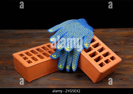 Briques rouges et gants en caoutchouc sur table en bois. Matériau de construction Banque D'Images