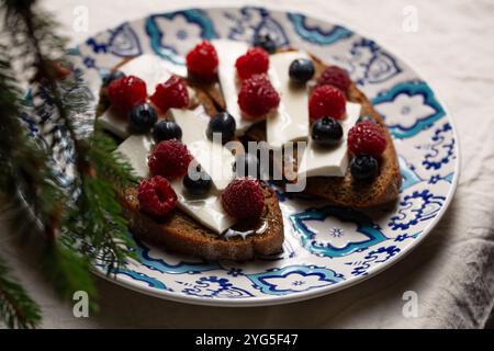 Deux sandwichs avec fromage de chèvre, framboises et bleuets sur une assiette avec des motifs près du sapin de Noël Banque D'Images