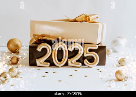 Conception de vue de face de célébration avec des numéros dorés 2025, près de la boîte cadeau avec des décorations festives, des étoiles d'or confettis et la création d'un vibrant et joyeux Banque D'Images
