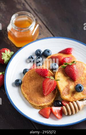 Crêpes avec fraises, bleuets et miel sur assiette, fond de table en bois brun. Gros plan Banque D'Images