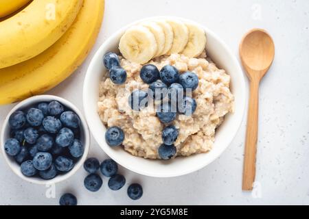 Gruau de porridge avec des bleuets et des bananes dans un bol, vue sur table. Repas de petit-déjeuner végétalien sain Banque D'Images