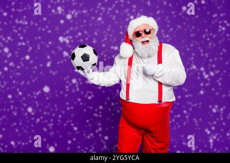 Photo de grey haired santa avec ballon de football en cuir de démonstration de nouveaux modèle football ball pour escompte x-mas : porter un costume specs sun Banque D'Images