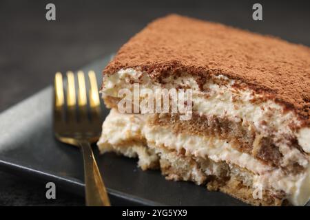 Morceau de savoureux tiramisu et fourchette sur la table noire, gros plan Banque D'Images